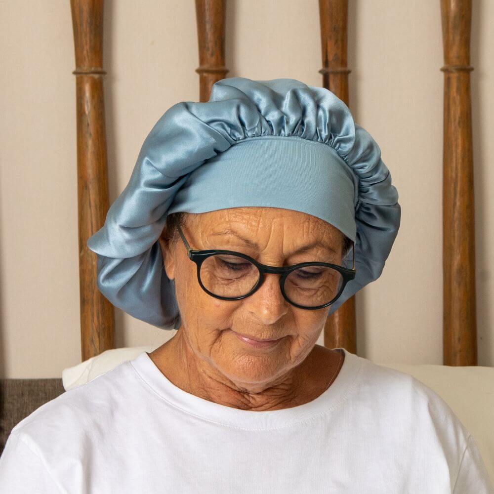 An old woman wearing eyeglasses and stale silk hair bonnet on a cream with babboo woods in the background