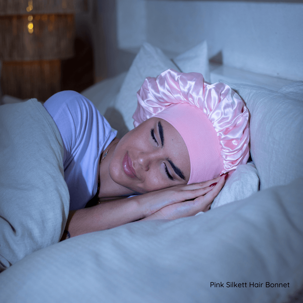 A woman sleeping on her side while wearing a pink silk bonnet